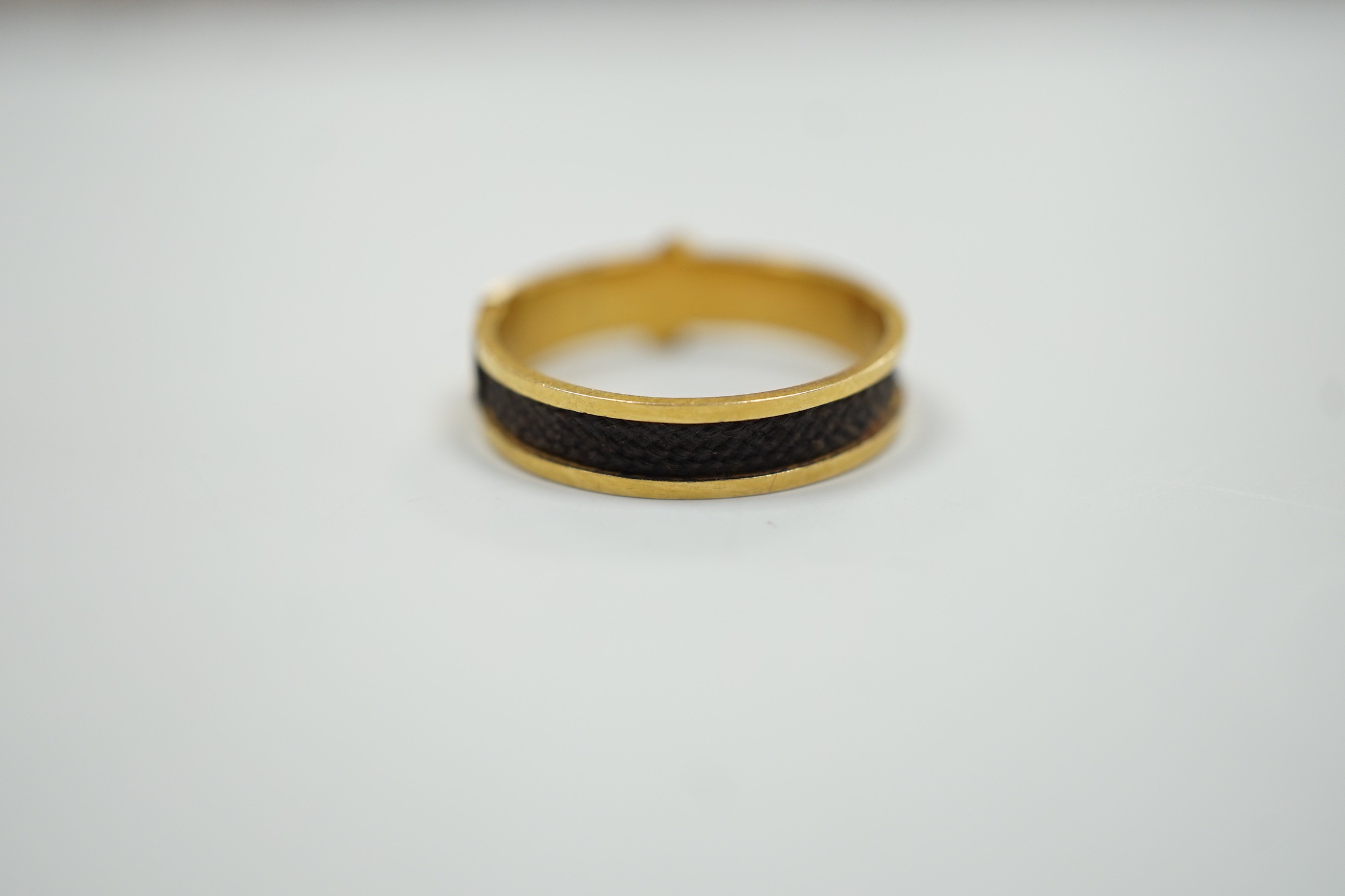 A 19th century yellow metal and plaited hair mourning band, modelled as a buckle, the shank interior engraved with the initials JDS?, size O/P, gross weight 2.1 grams.